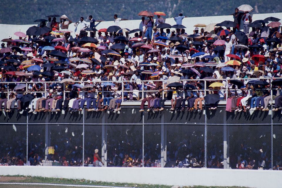 Spectators in Jamaica shield themselves from the sun with umbrellas, 1986