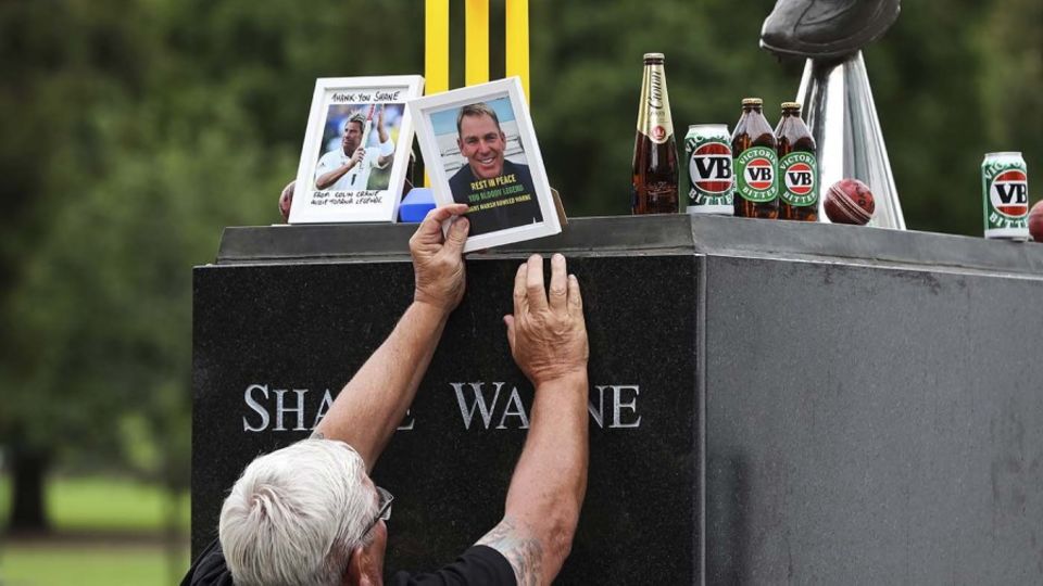A man places a set of stumps at Shane Warne's statue at the MCG