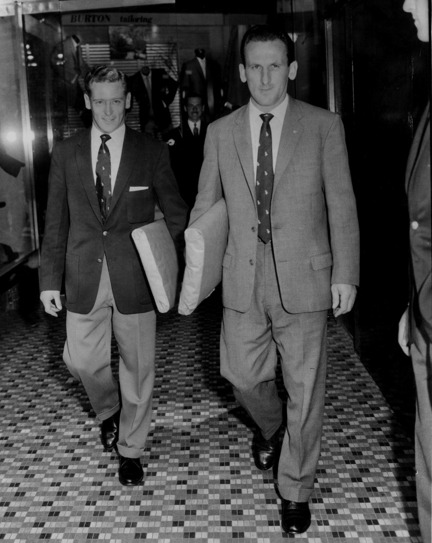 Jackie McGlew and Sid O'Linn walk out of a tailoring store in their new suits