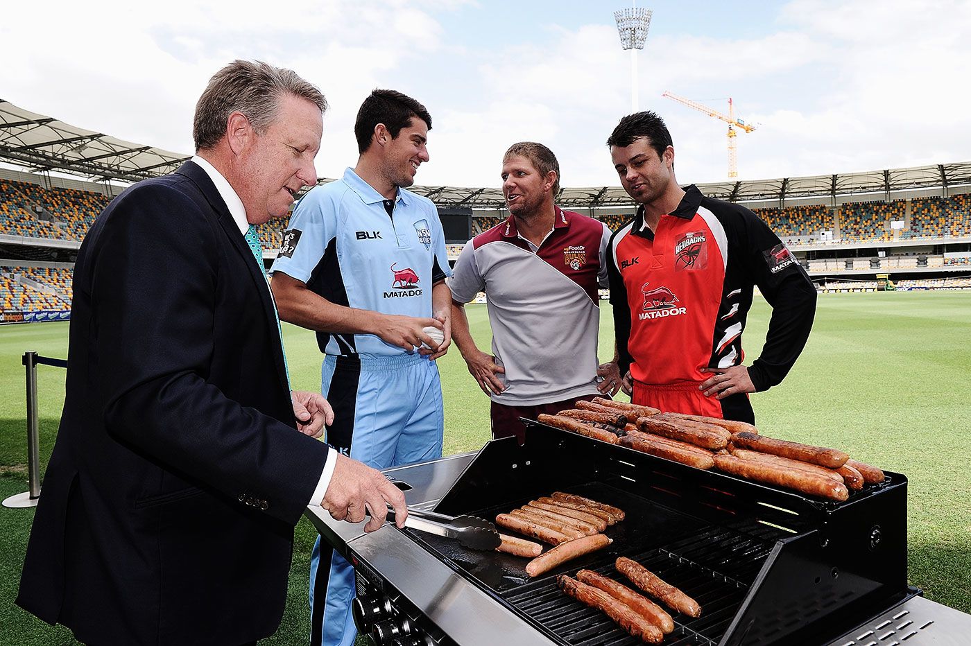 Moises Henriques, James Hopes and Callum Ferguson watch Ian Healy cook sausages