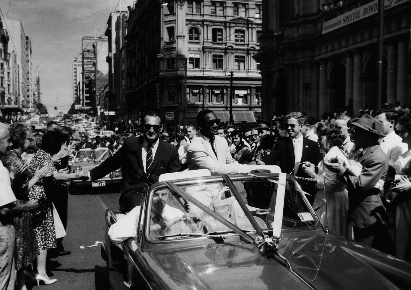 Gerry Gomez and Frank Worrell sit in an open-top car and drive through the streets of Melbourne greeting fans who came to see off the West Indies side at the end of the tour
