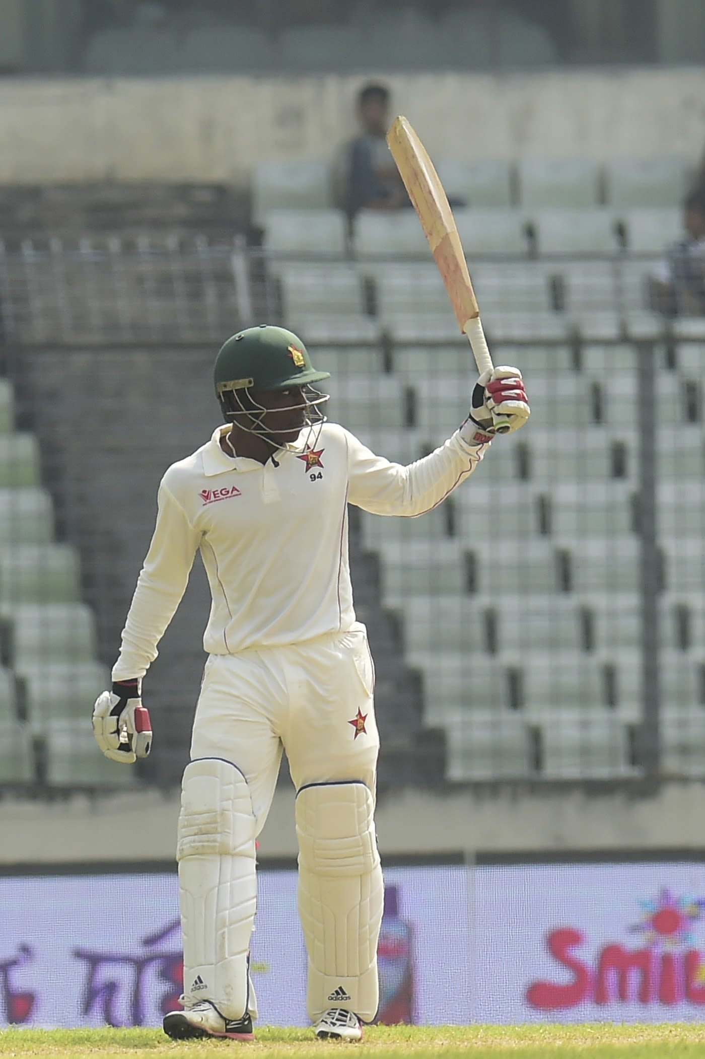 Brian Chari raises his bat after reaching a half-century