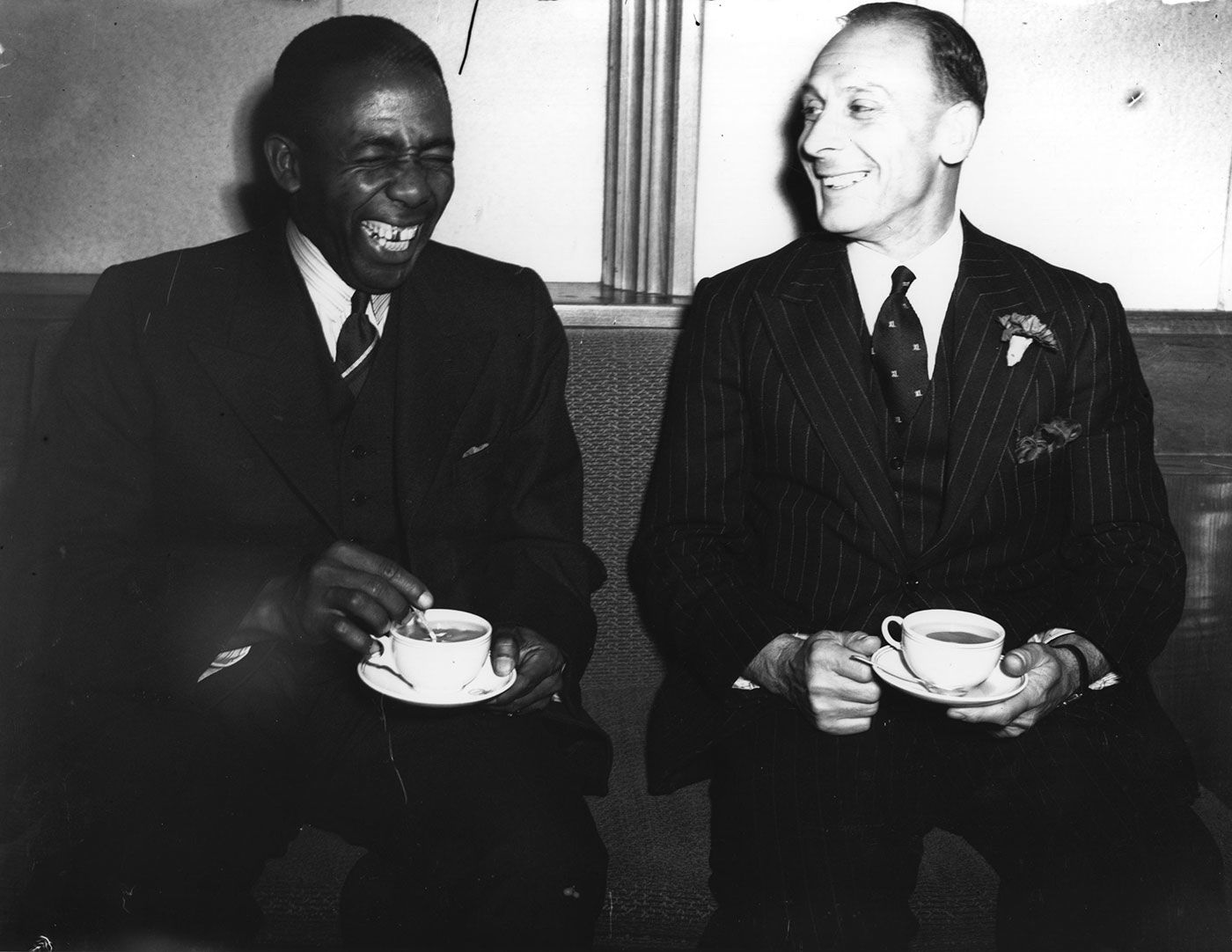 Learie Constantine and Jack Hobbs laugh over cups of tea at a reception to welcome the West Indies team