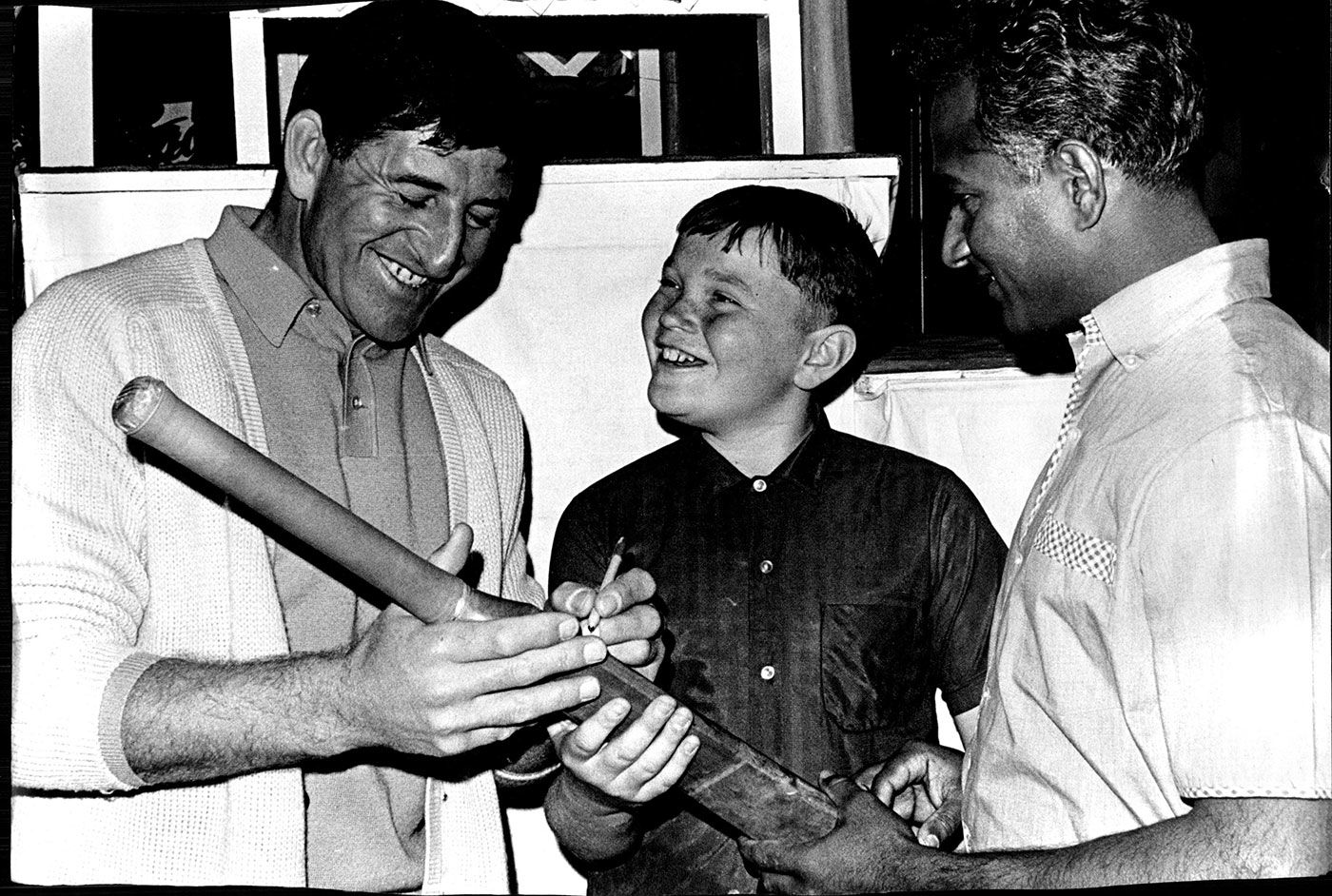 Ken Barrington (left) and Rohan Kanhai sign autographs for a boy in Sydney