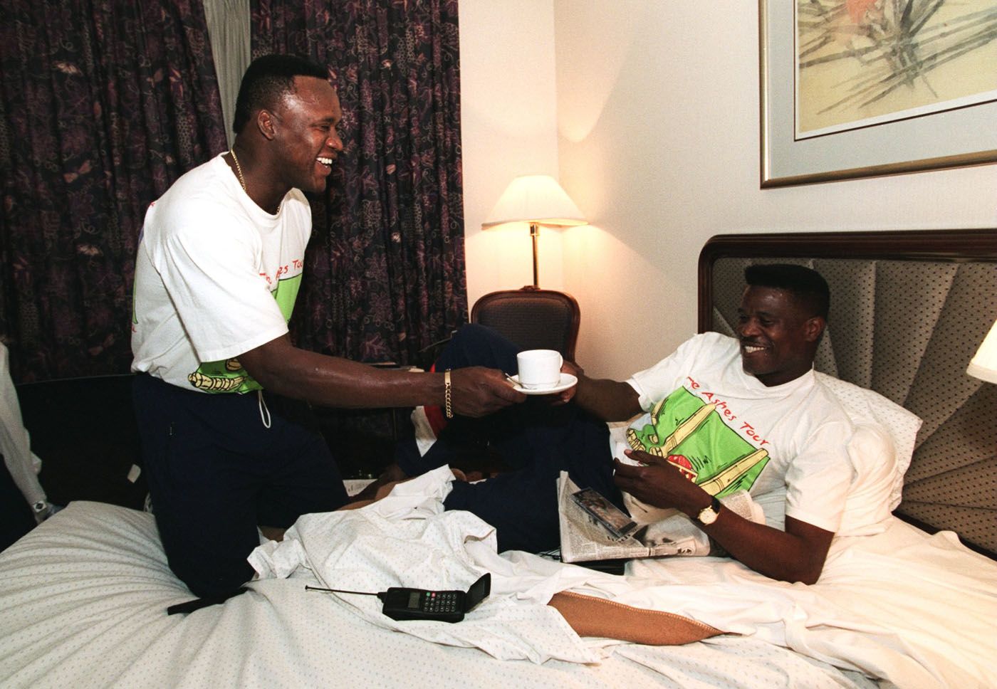 Devon Malcolm offers a cup of tea to his chicken-pox-afflicted team-mate Joey Benjamin in his hotel room