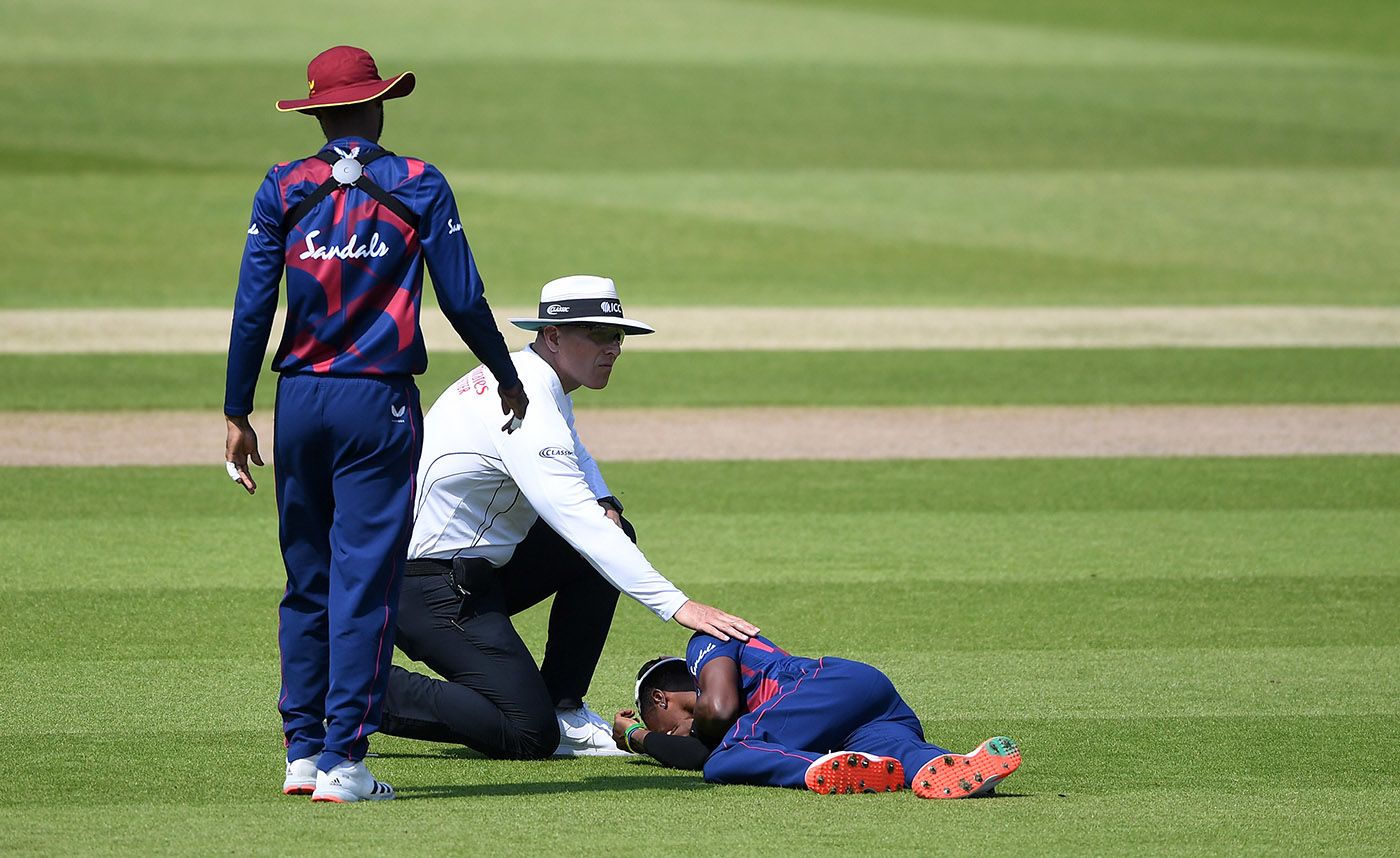 Umpire Alex Wharf checks on Keon Harding, who was injured while attempting to field the ball