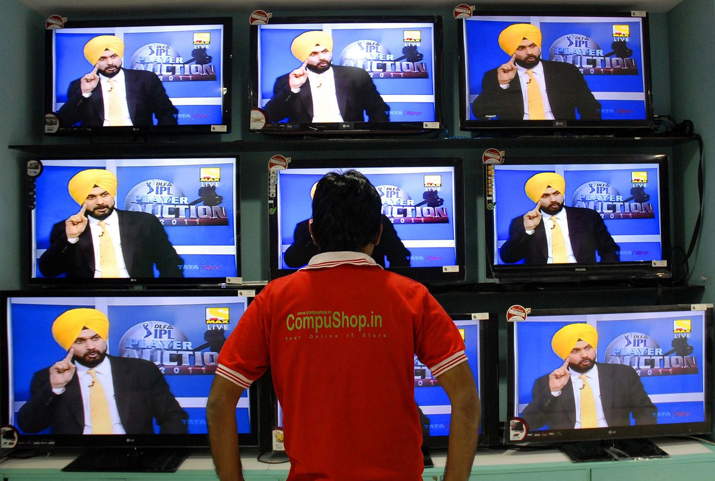 A man watches the IPL auction on a bank of television sets