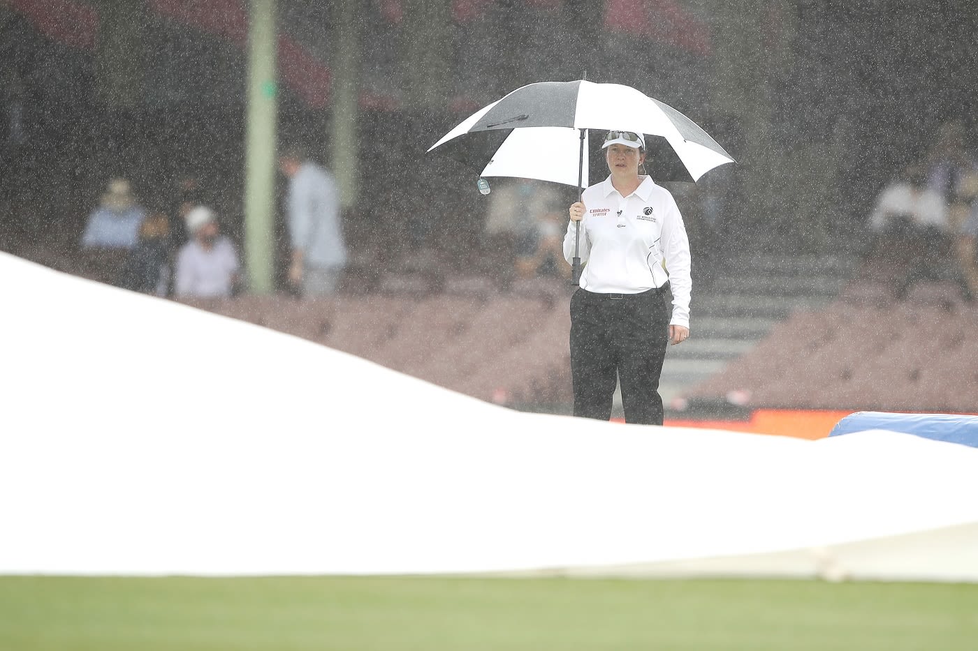 Reserve umpire Claire Polosak watches on as ground staff cover the pitch during a rain delay