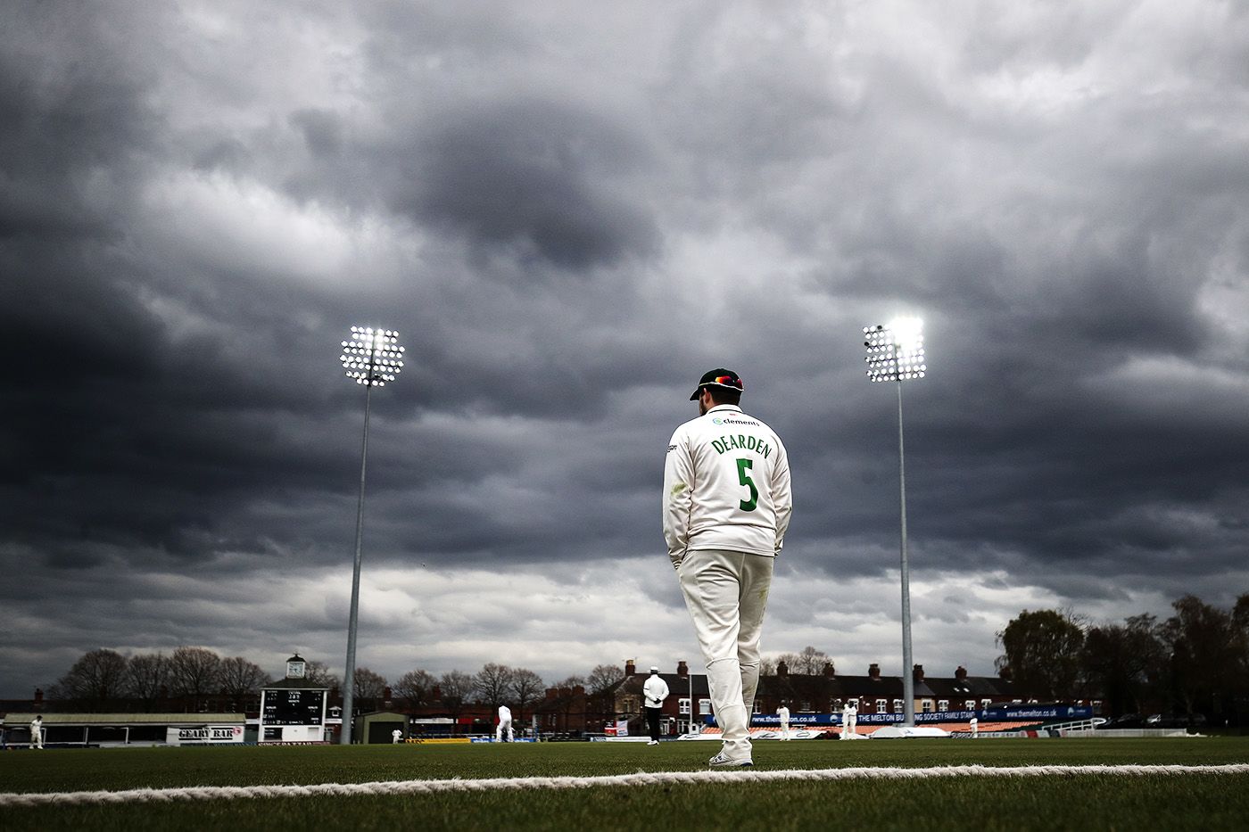 Leicestershire's Harry Dearden stands at the boundary with his hands in his pockets as dark clouds gather in the sky