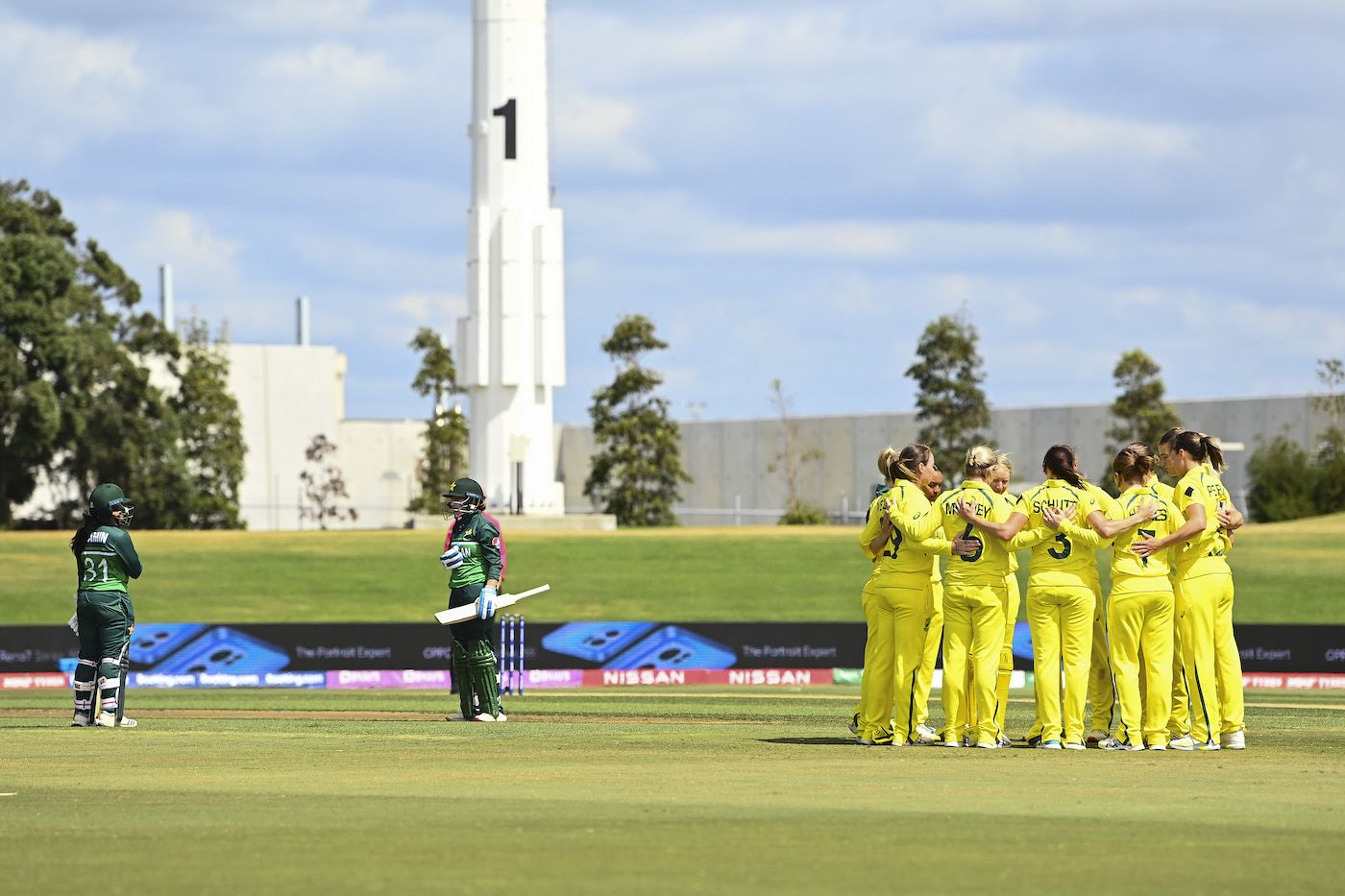 Australia get into a huddle while Sidra Ameen and Nahida Khan get ready