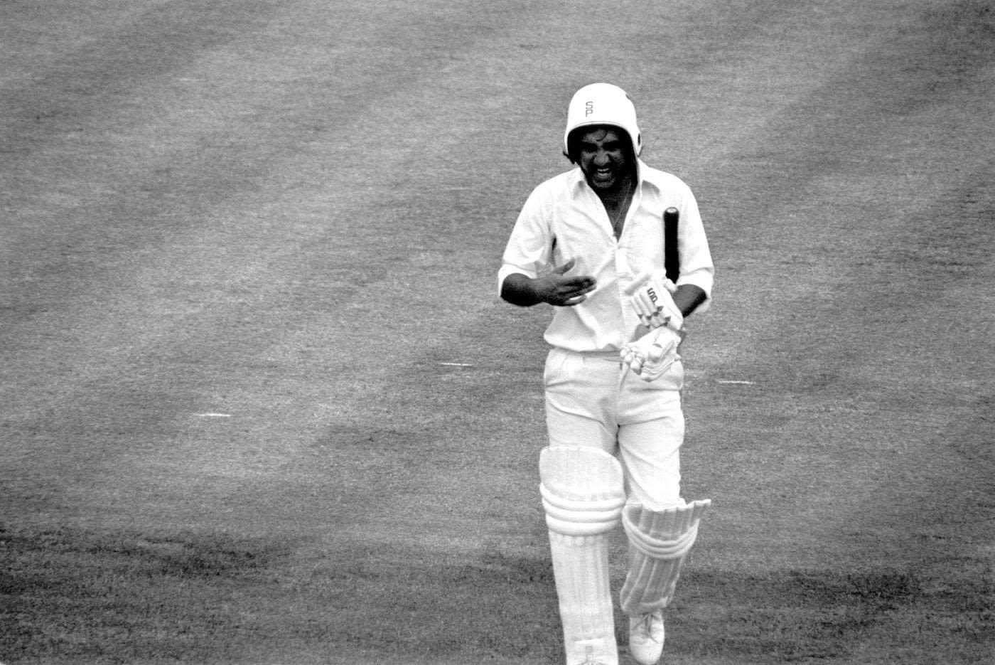 Sadiq Mohammad, wearing an unusually styled helmet, walks back to the pavilion after being dismissed