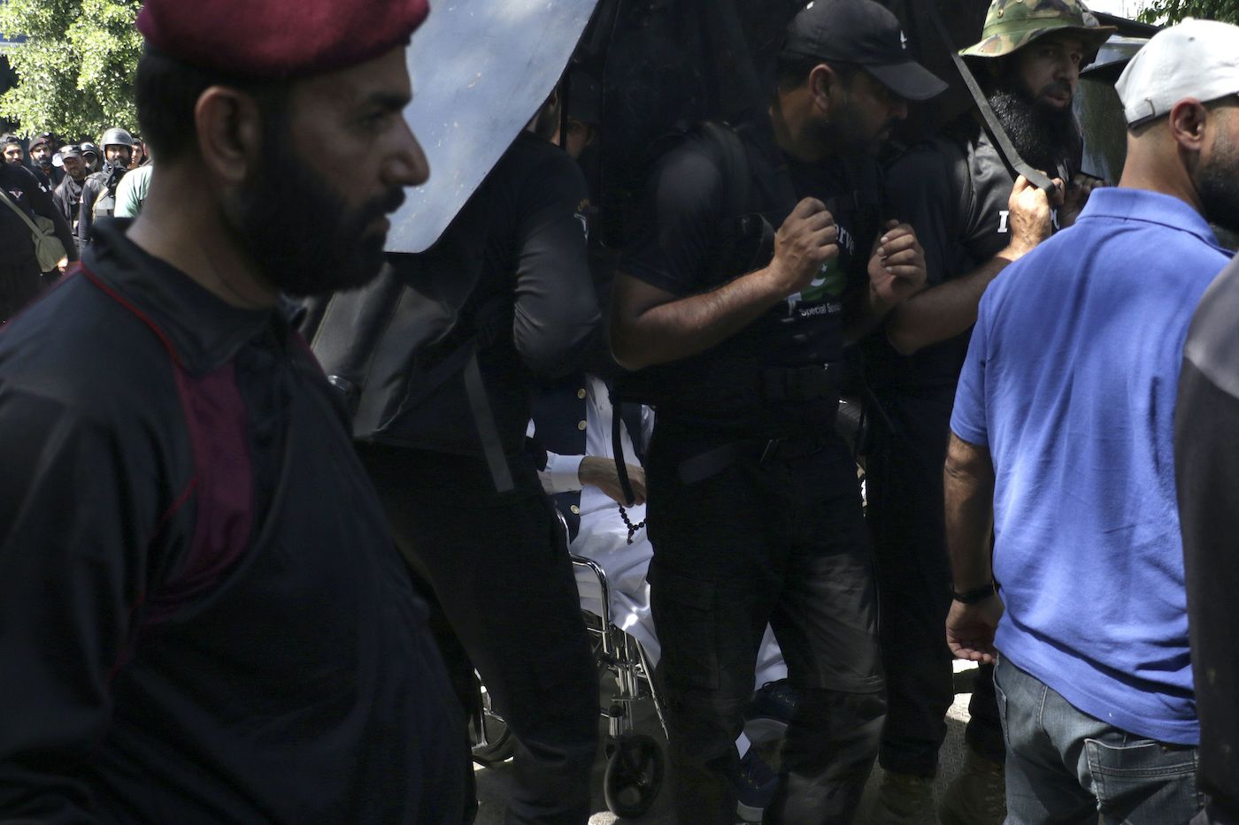 Private security personnel escort Imran Khan, in a wheelchair, as he arrives to appear in a court, in Islamabad