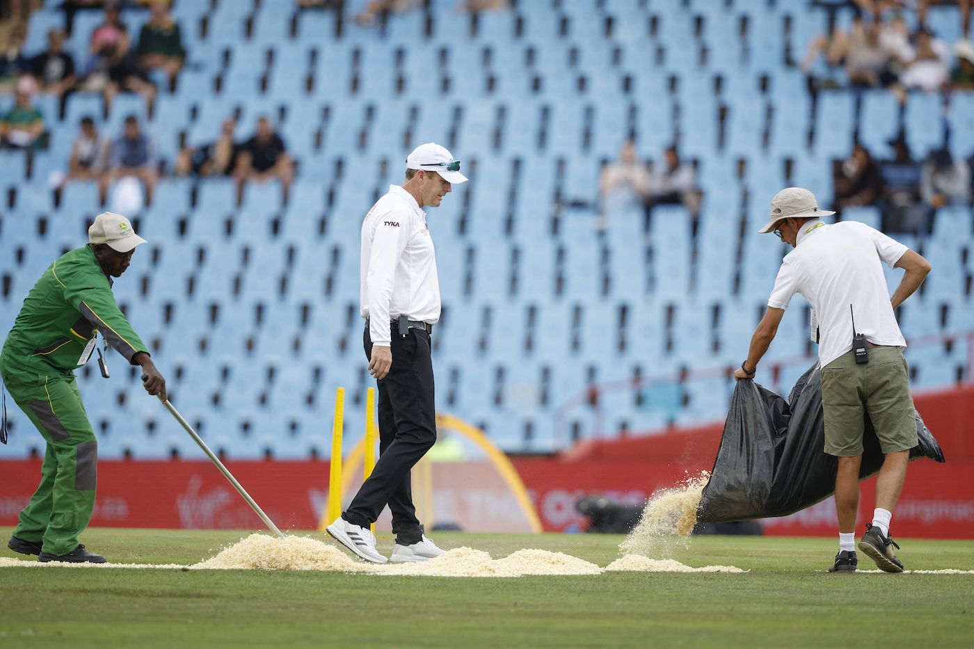 Groundsmen use sawdust on the field as Stephen Harris looks on