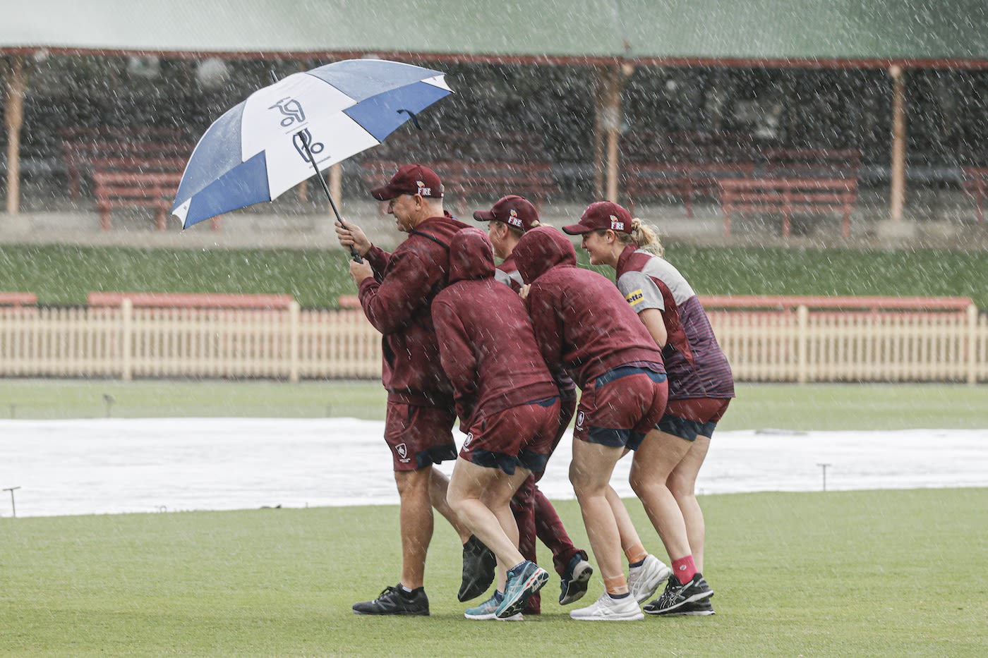 Queensland Coach Scott Prestwidge shelters players as they inspect the ground in the rain