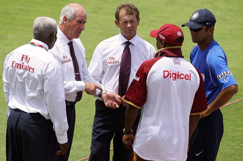 The umpires have a chat with the two captains as wet weather delays the start of play