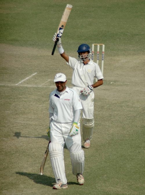 Uday Kaul raises his bat upon reaching his century while Pankaj Dharmani looks on