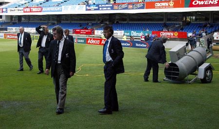 Match officials check the condition of wet patches in the outfield on the third morning