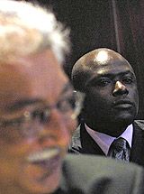 Maurice Odumbe stands behind his lawyer